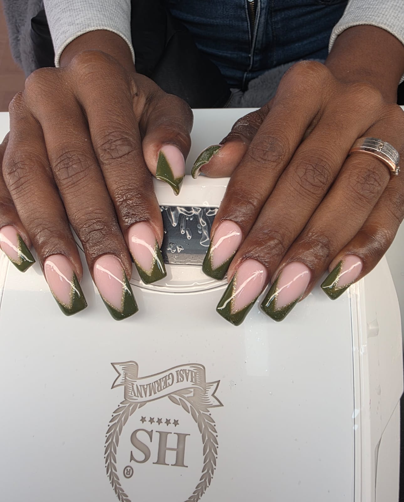 Lange kunstnagels met een olijfgroene French, handen op een witte nagelkoffer