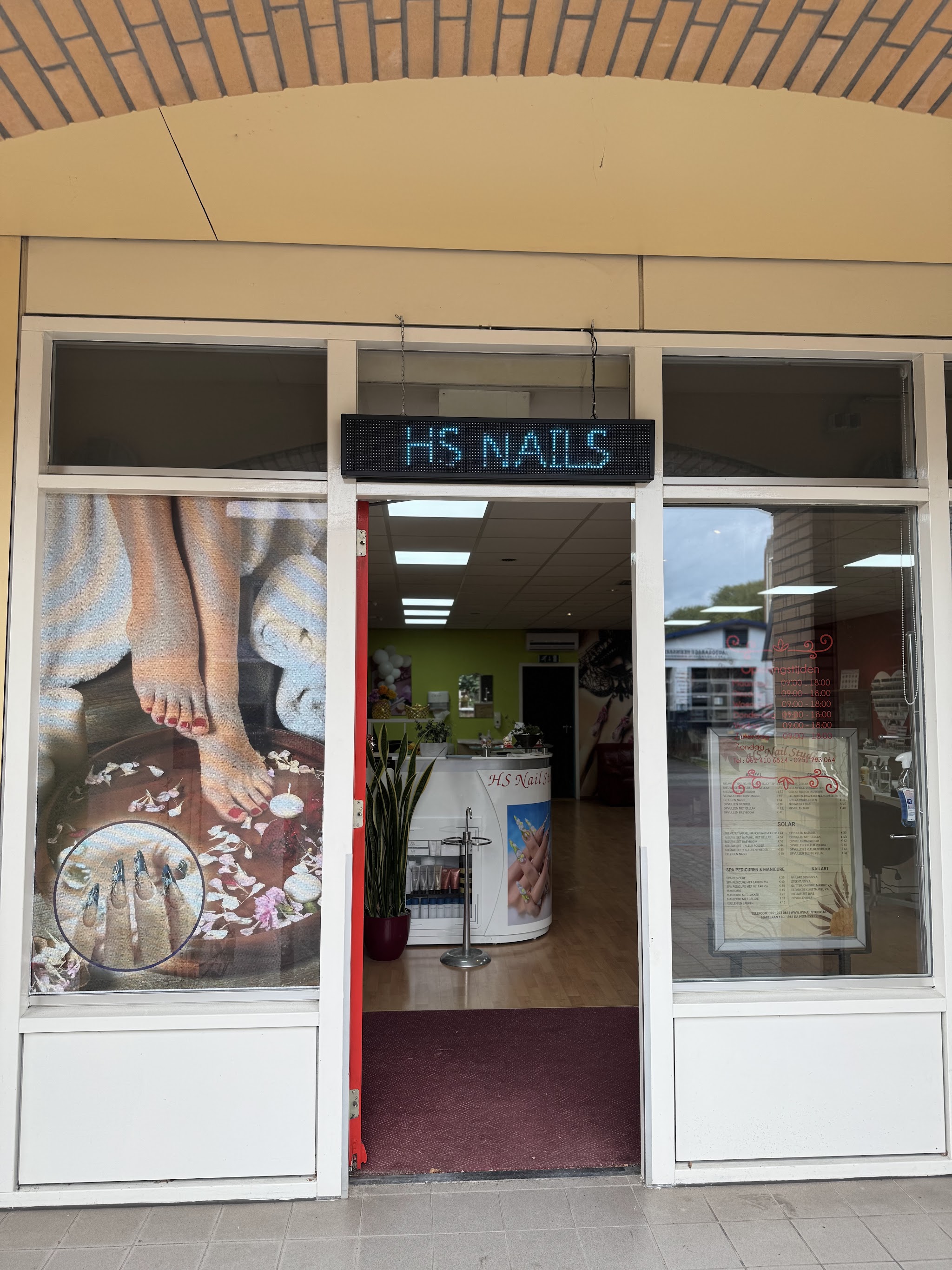 De ingang van HS Nail Studio met grote ramen en een lichtbord boven de deur